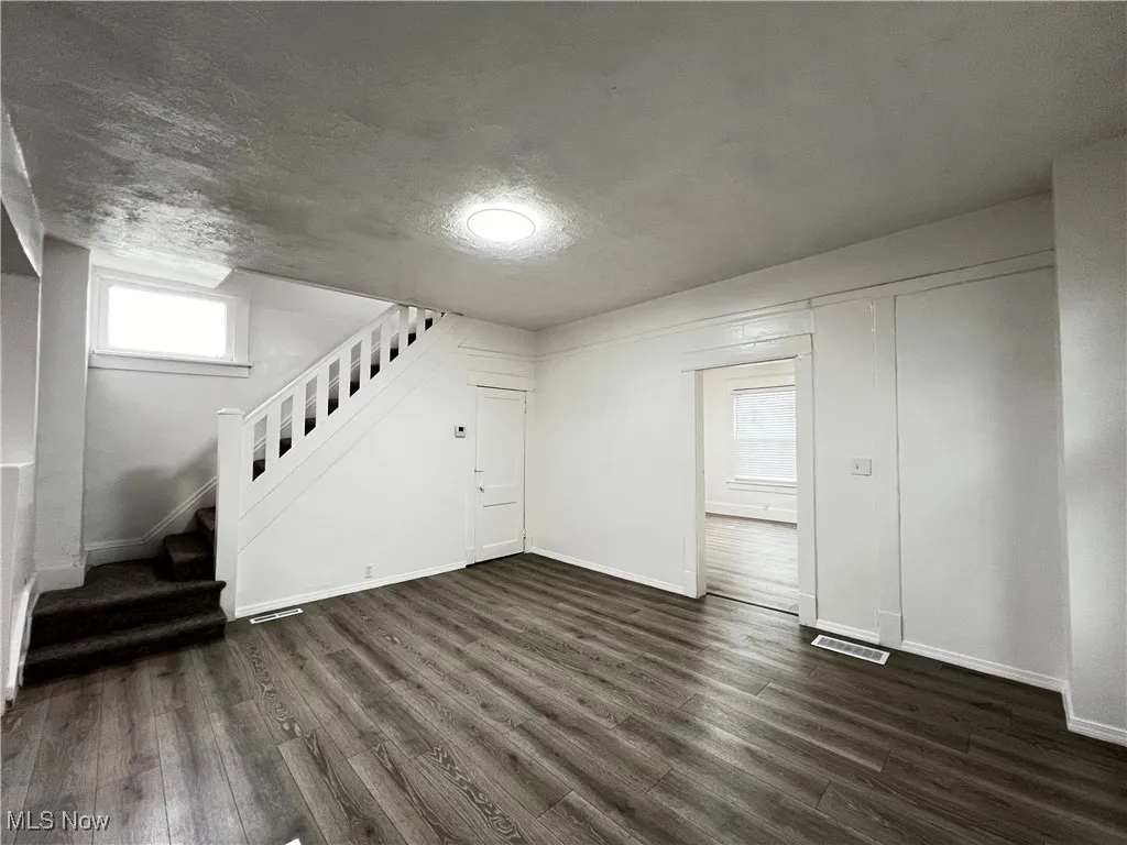 Unfurnished living room featuring stairs, dark wood-style flooring, and a textured ceiling
