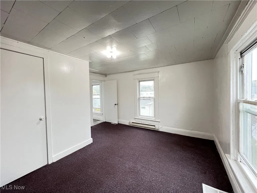 Unfurnished room featuring dark colored carpet and baseboard heating