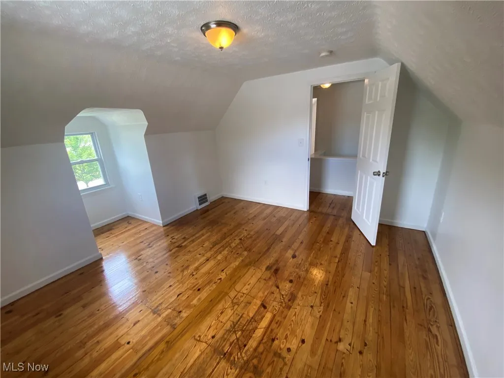 Bonus room with a textured ceiling, hardwood / wood-style flooring, and vaulted ceiling