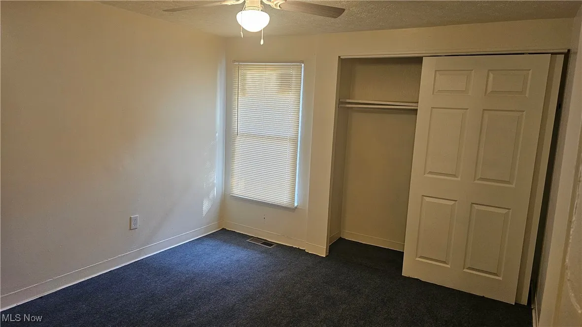 Unfurnished bedroom featuring a textured ceiling, dark carpet, ceiling fan, and a closet