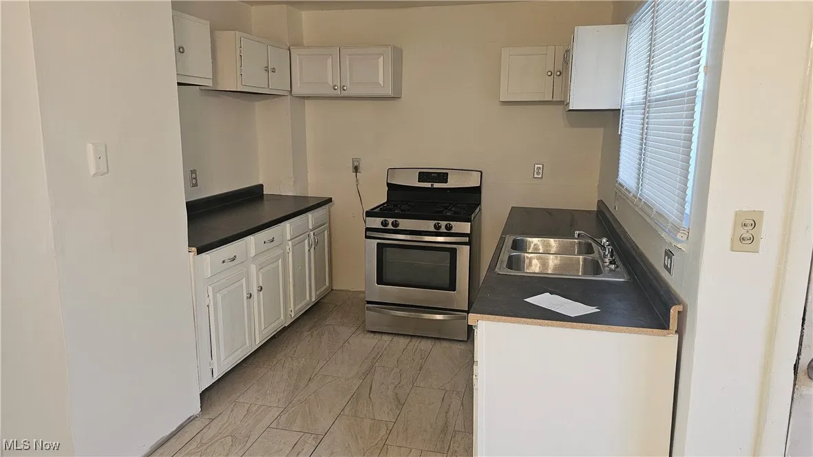 Kitchen featuring stainless steel range with gas stovetop, white cabinets, and dark countertops