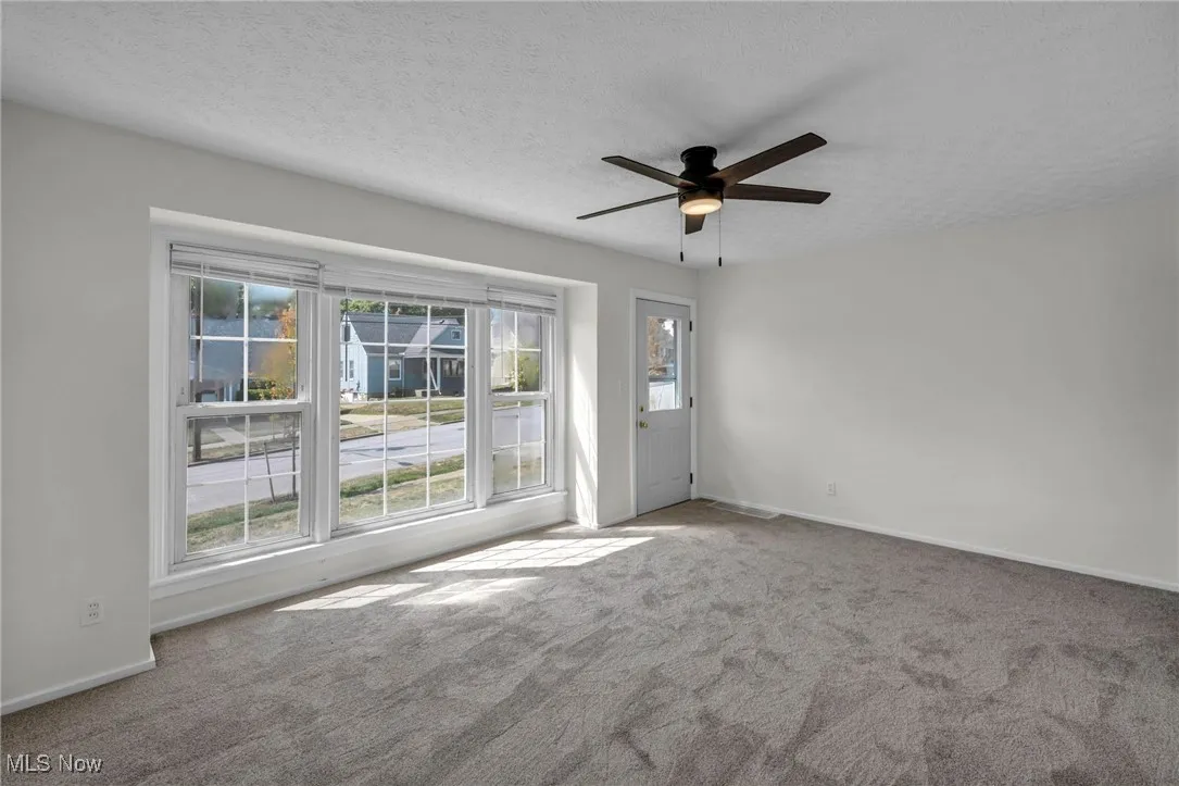 Empty room with healthy amount of natural light, a textured ceiling, a ceiling fan, and carpet