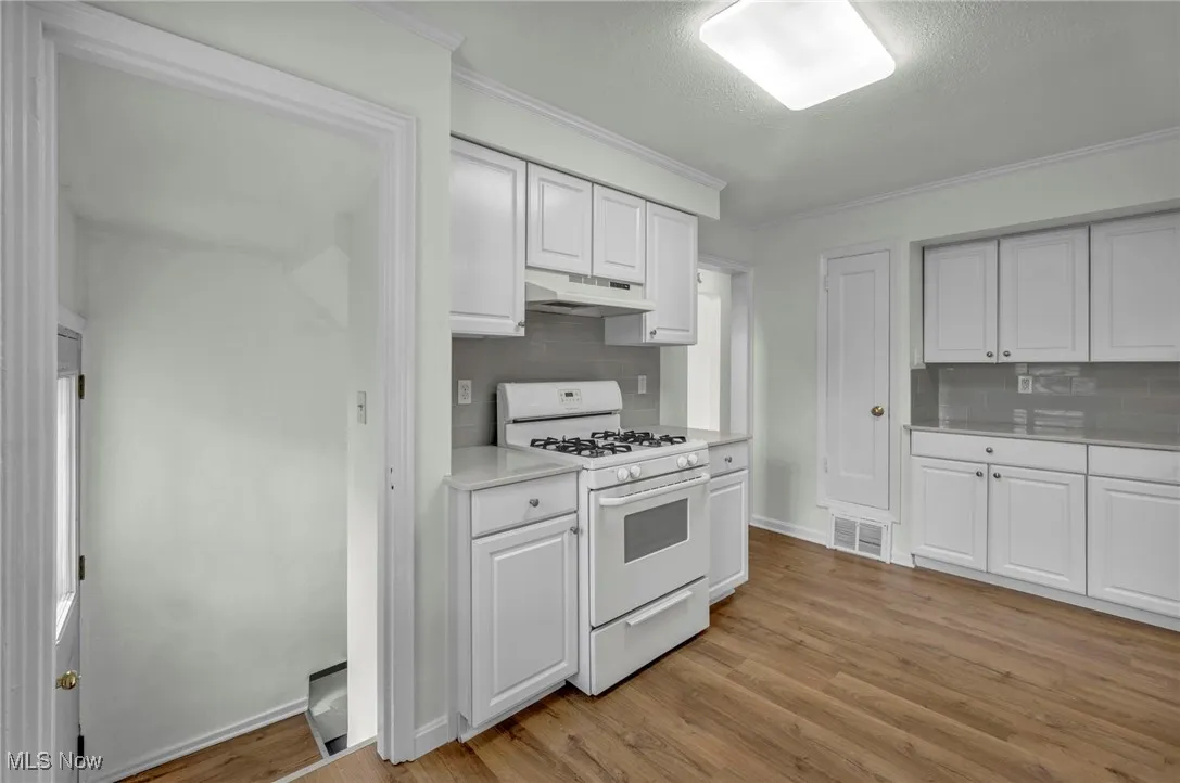 Kitchen with white range with gas stovetop, light countertops, white cabinetry, light wood-style floors, and ornamental molding