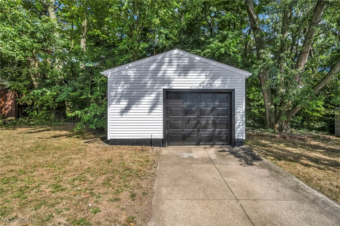 Detached garage featuring concrete driveway and view of scattered trees