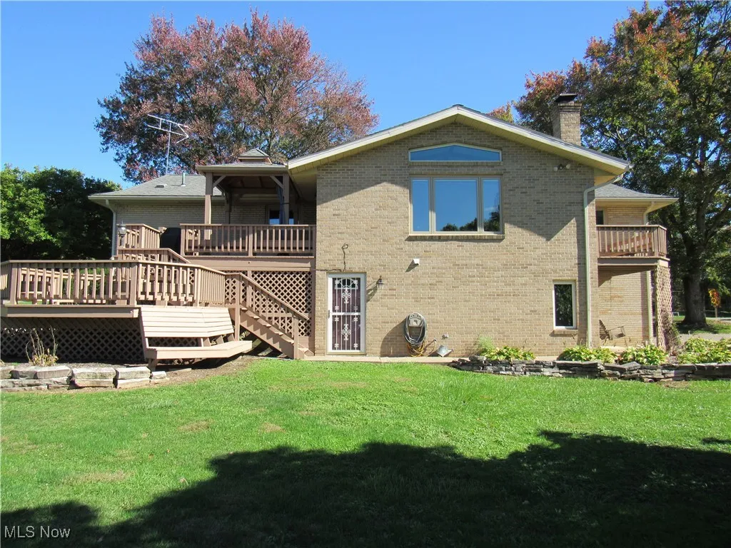 Rear view of house featuring a chimney, a lawn, brick siding, and 3 wooden deck