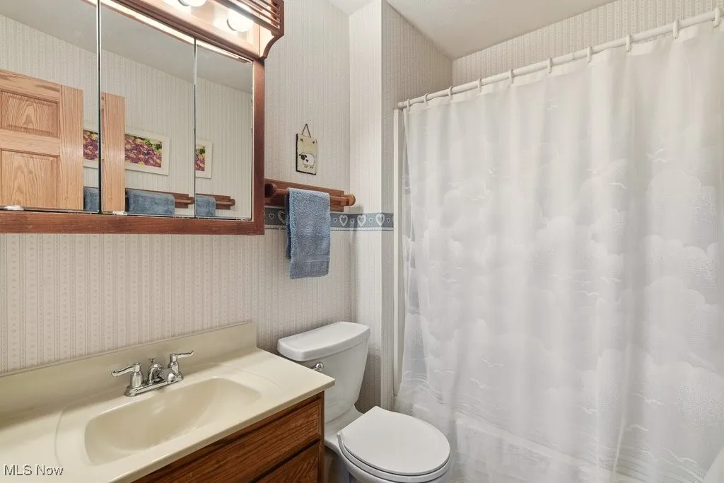 Full bathroom featuring wallpapered walls and vanity