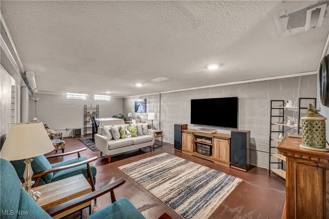 Living room with concrete block wall, concrete flooring, and a textured ceiling
