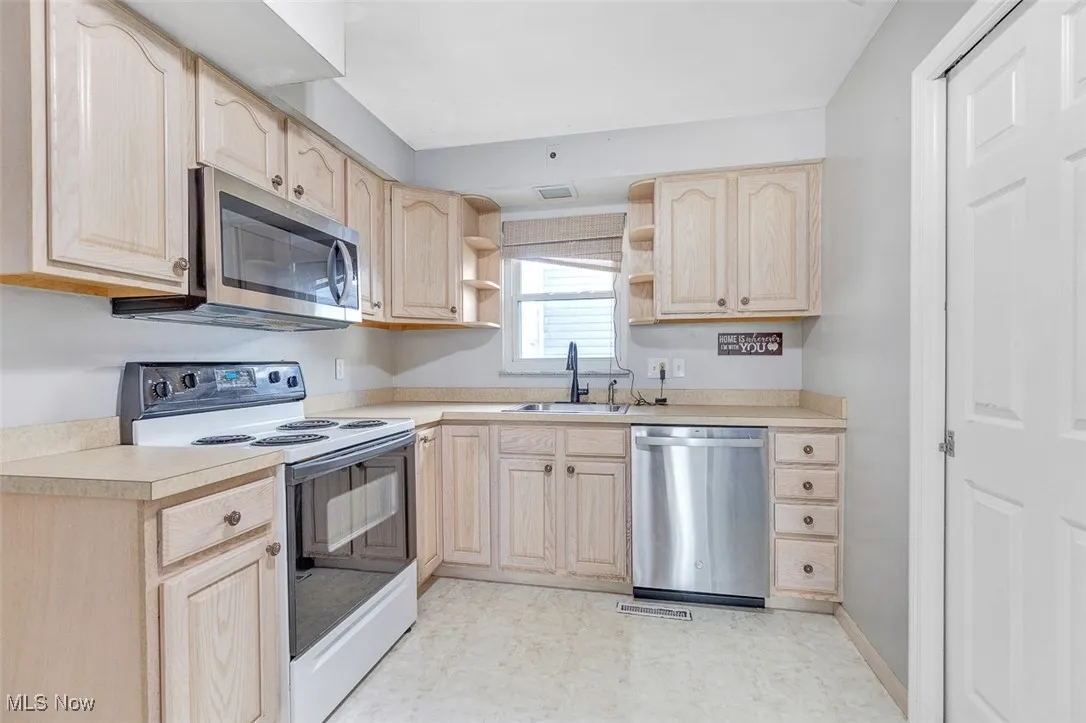 Kitchen featuring light brown cabinetry, stainless steel appliances, open shelves, and light countertops