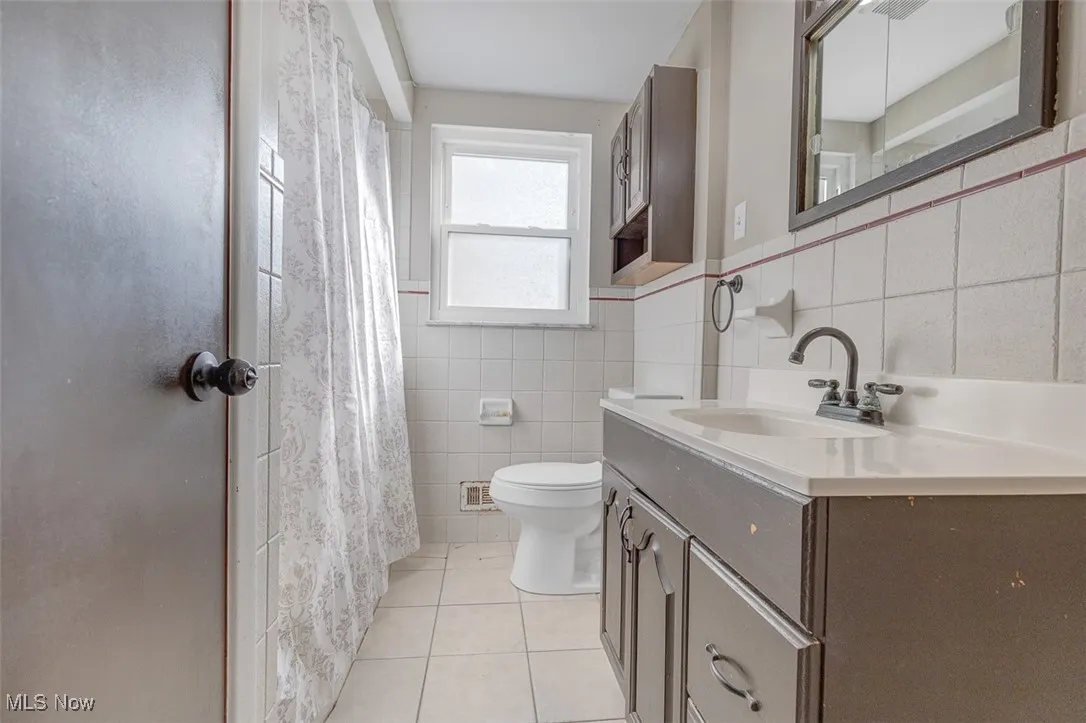 Bathroom with light tile patterned floors, tile walls, vanity, and a shower with curtain