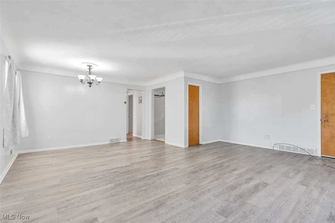 Empty room with light wood-type flooring and a chandelier