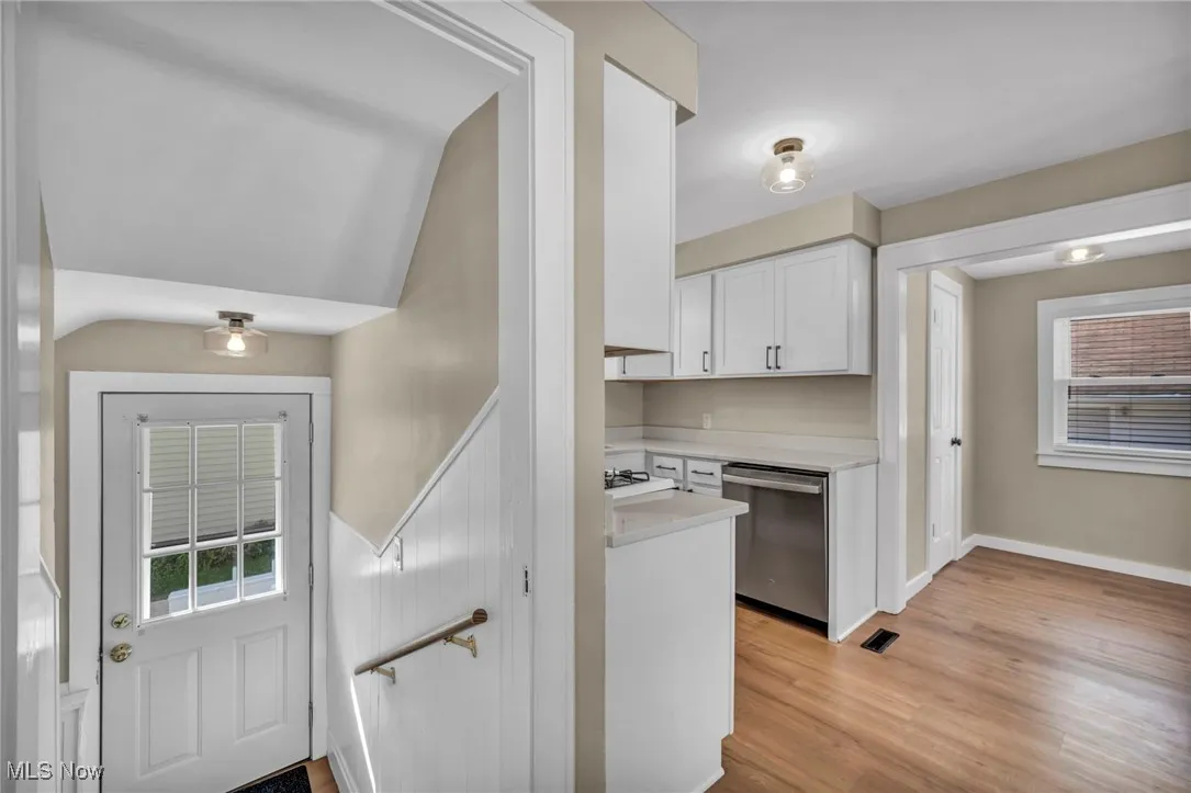 Kitchen with plenty of natural light, white cabinets, stainless steel dishwasher, and light wood finished floors