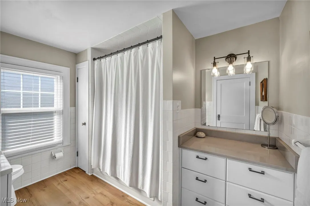 Bathroom featuring tile walls, light wood-style flooring, vanity, and a shower with curtain
