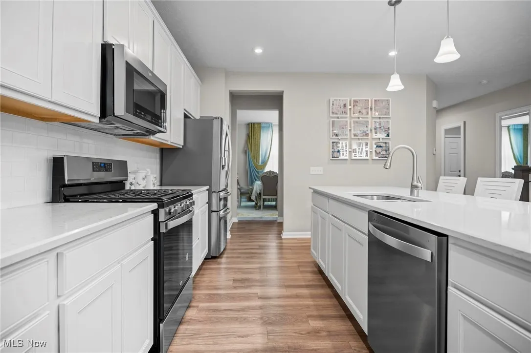 Kitchen with appliances with stainless steel finishes, white cabinets, light stone counters, decorative backsplash, and light wood-style flooring
