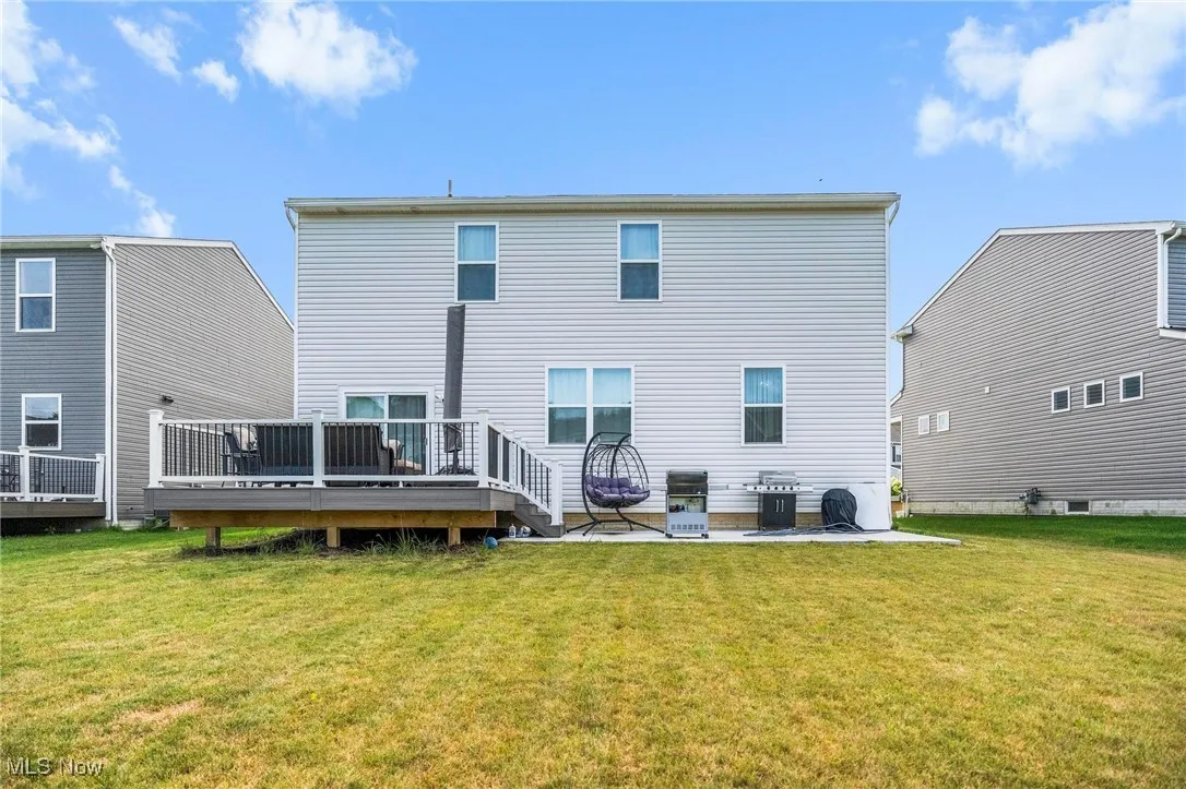 Back of property with a lawn, a deck, and a patio