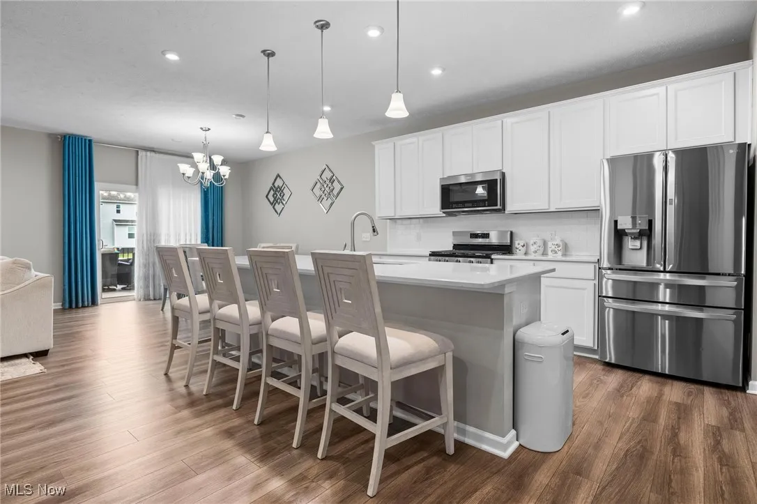 Kitchen featuring stainless steel appliances, a kitchen breakfast bar, white cabinets, a center island with sink, and recessed lighting