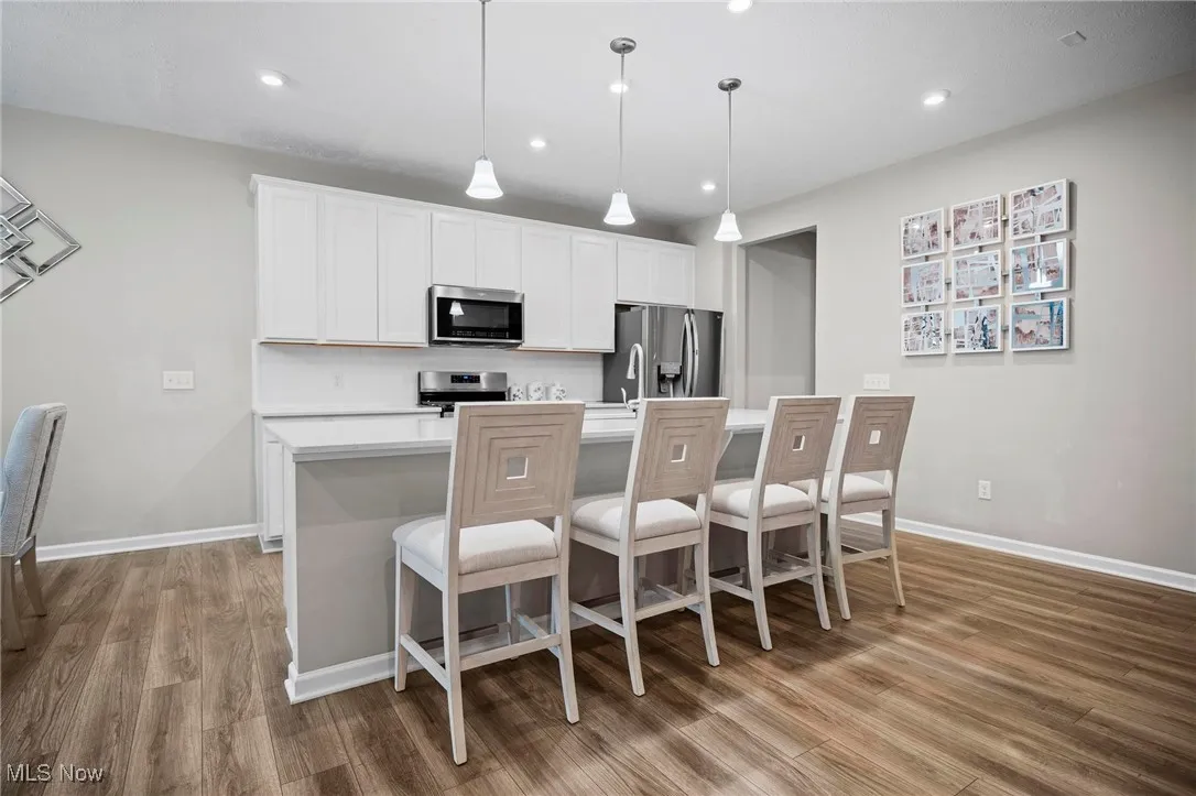 Kitchen featuring pendant lighting, stainless steel appliances, a breakfast bar, white cabinets, and an island with sink