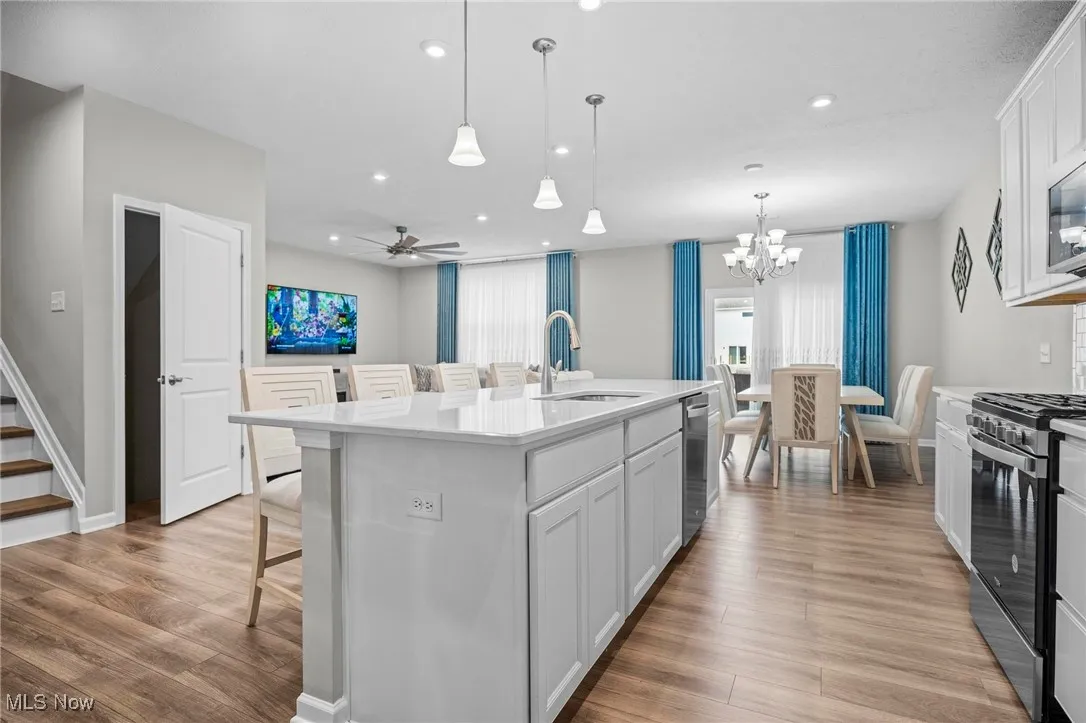 Kitchen featuring white cabinets, a kitchen bar, decorative light fixtures, a center island with sink, and appliances with stainless steel finishes