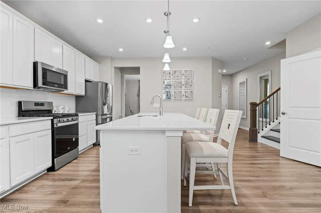 Kitchen with appliances with stainless steel finishes, white cabinets, light wood-type flooring, hanging light fixtures, and recessed lighting