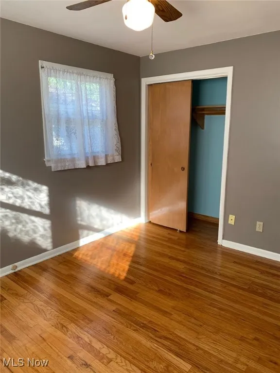 Unfurnished bedroom with wood finished floors, a closet, and a ceiling fan