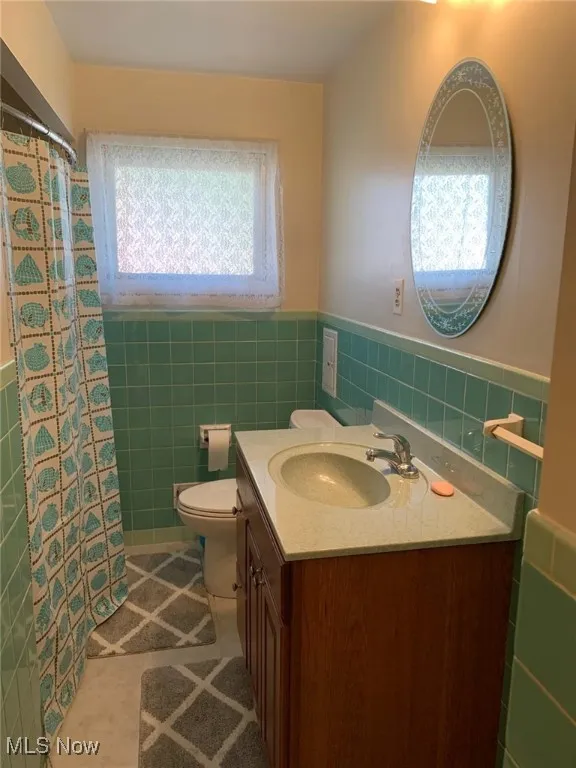 Bathroom featuring tile walls, vanity, tile patterned flooring, a wainscoted wall, and curtained shower