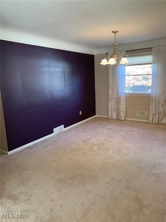 Spare room featuring light colored carpet and a chandelier