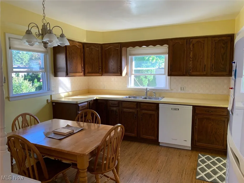 Kitchen with light countertops, white appliances, light wood finished floors, pendant lighting, and a chandelier