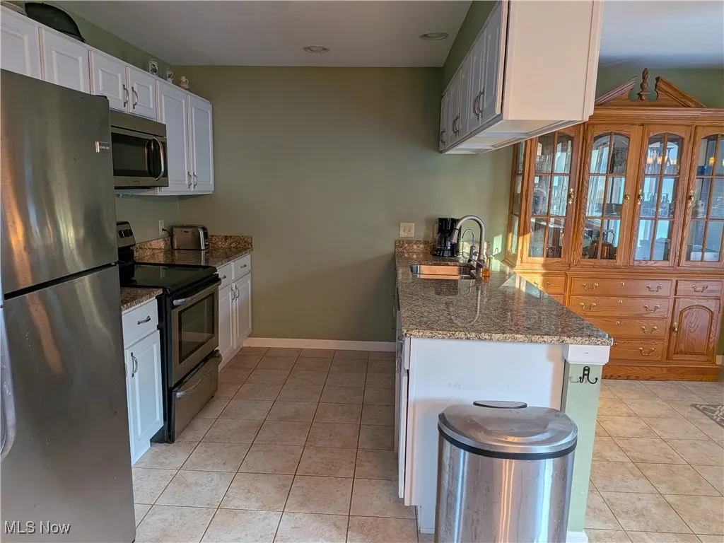Kitchen featuring stainless steel appliances, dark stone counters, light tile patterned floors, and a peninsula