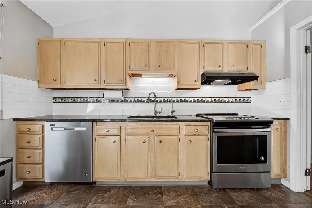 Kitchen featuring light brown cabinetry, appliances with stainless steel finishes, decorative backsplash, and lofted ceiling