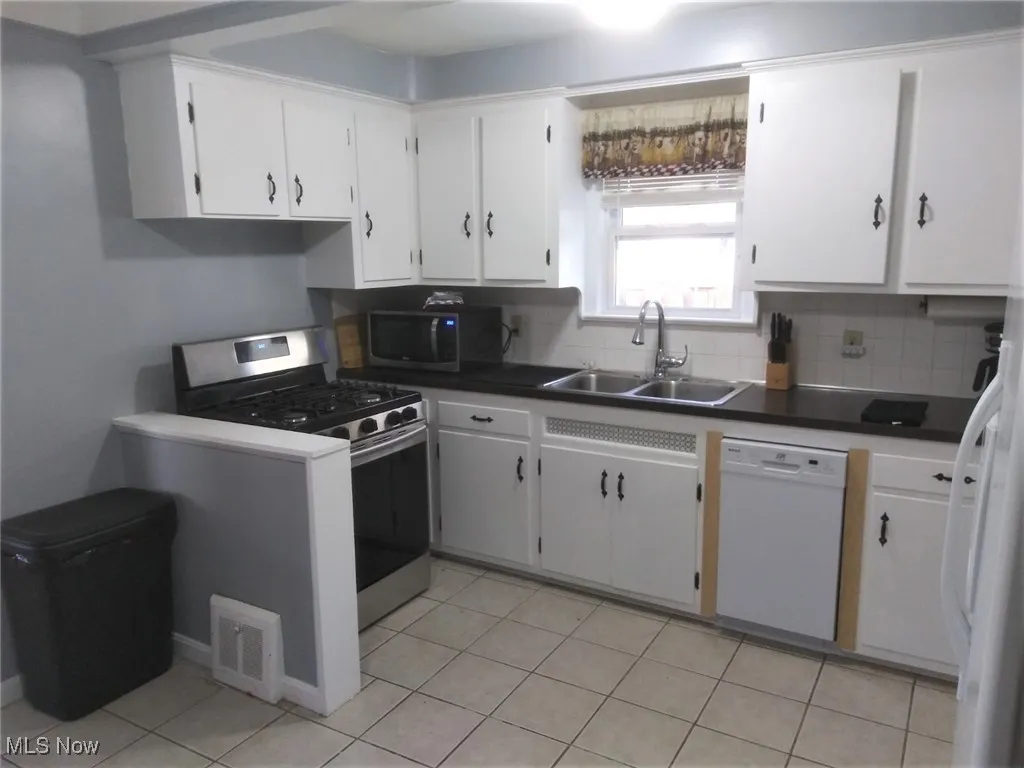Kitchen featuring stainless steel appliances, backsplash, and white cabinetry