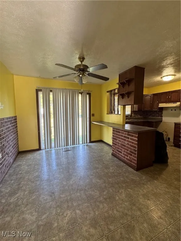 Living room featuring a textured ceiling, ceiling fan, and brick wall