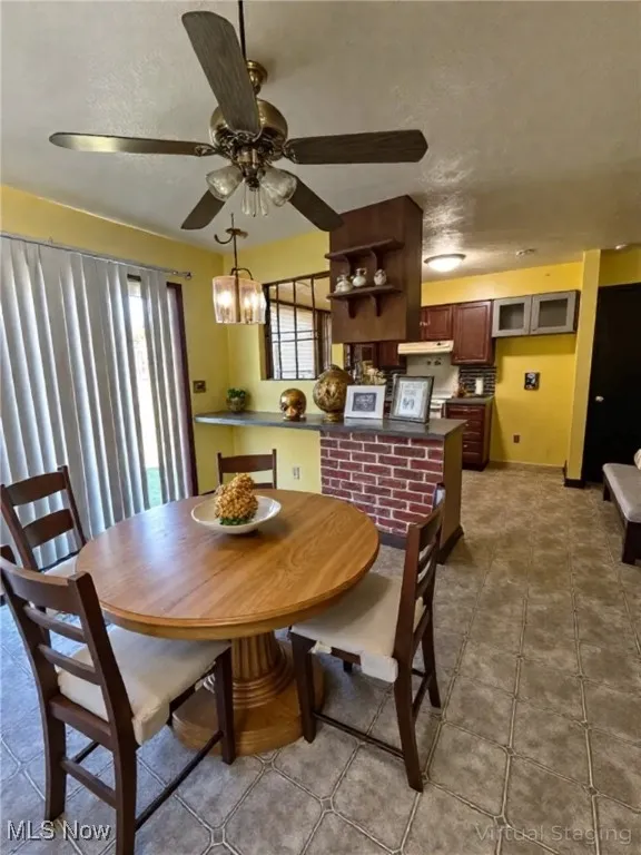 Tiled dining area with a textured ceiling, a ceiling fan, and a chandelier