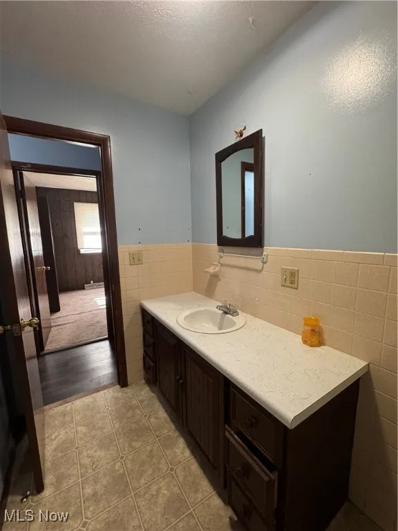 Bathroom with vanity, light tile patterned floors, tile walls, a textured ceiling, and a wainscoted wall