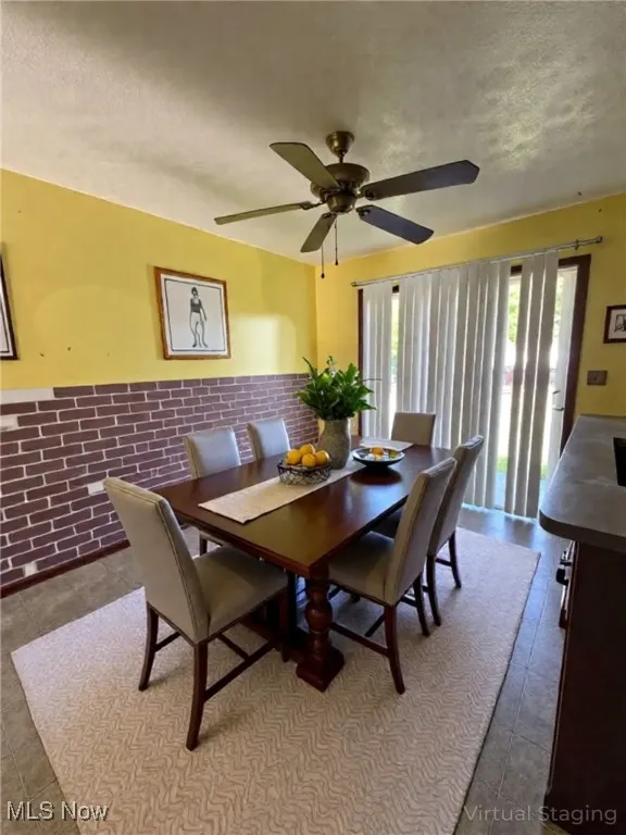 Dining room featuring wainscoting, a textured ceiling, a ceiling fan, tile walls, and dark tile patterned floors