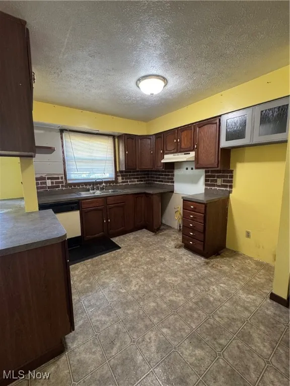 Kitchen with dark countertops, decorative backsplash, a textured ceiling, dishwashing machine, and dark brown cabinets