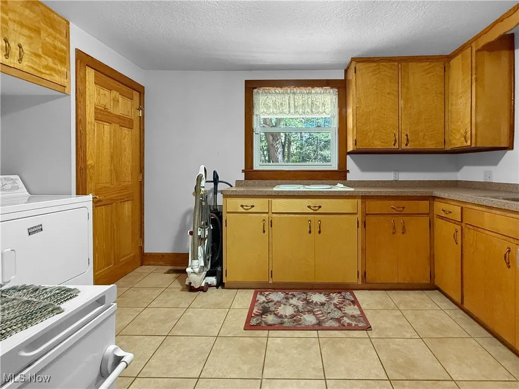 Kitchen with light tile patterned floors, washer / clothes dryer, a textured ceiling, and brown cabinets