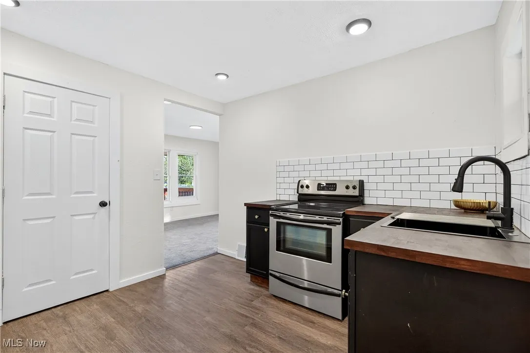 Kitchen featuring wood counters, electric range, decorative backsplash, dark cabinets, and dark wood finished floors