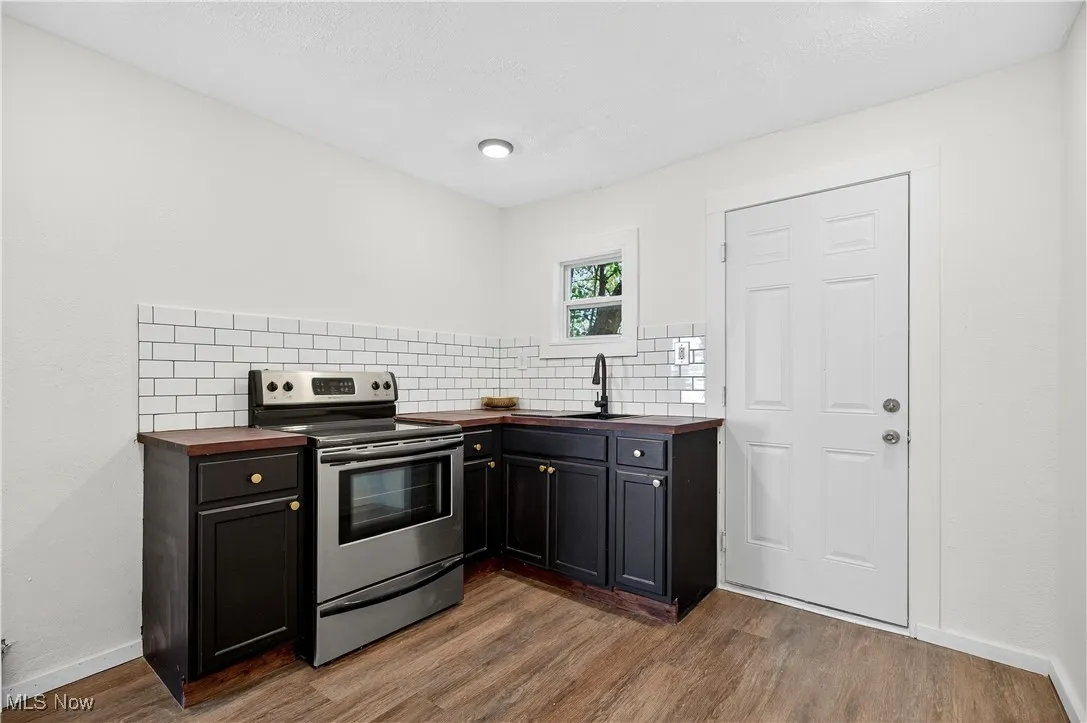 Kitchen with wooden counters, stainless steel range with electric cooktop, decorative backsplash, and dark wood-type flooring