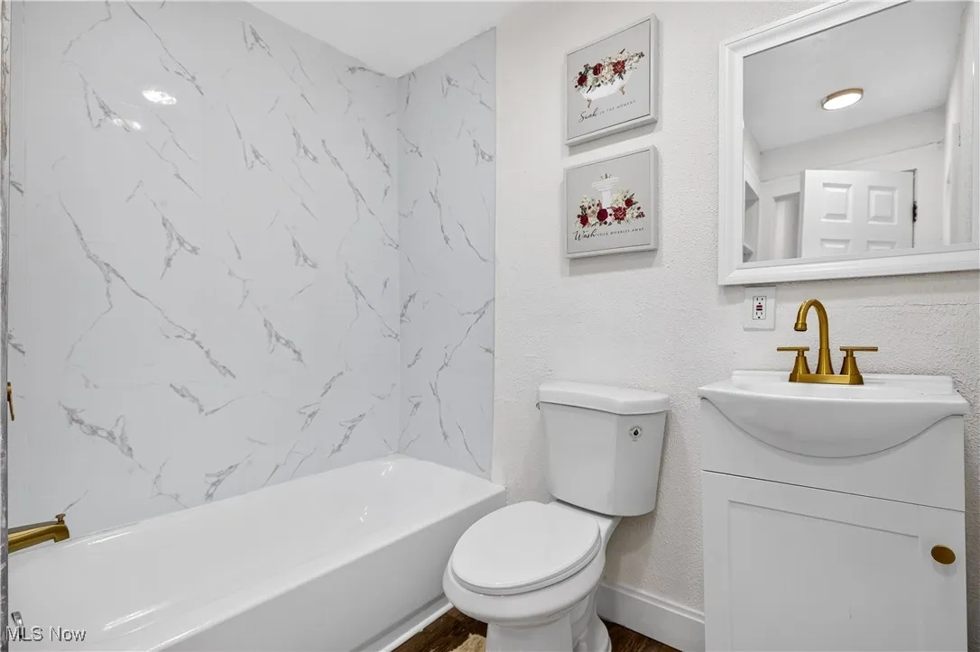 Bathroom featuring shower / bathtub combination, vanity, a textured wall, and wood finished floors