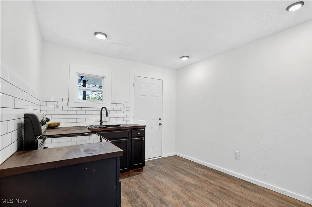 Kitchen featuring wooden counters, dark wood-type flooring, decorative backsplash, dark cabinets, and a textured ceiling