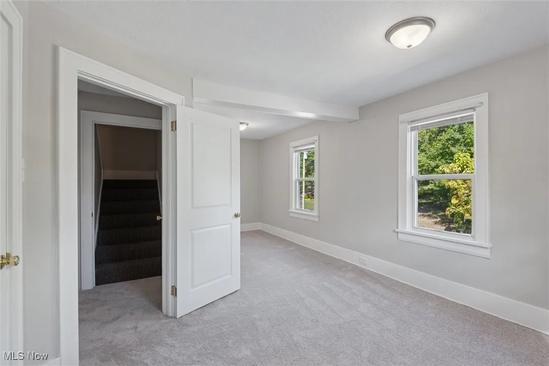 Unfurnished room featuring stairway and light carpet