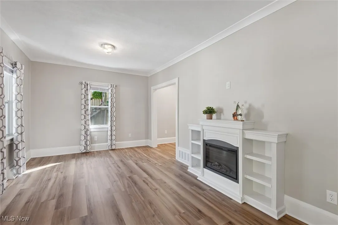 Unfurnished living room with a glass covered fireplace, crown molding, and wood finished floors