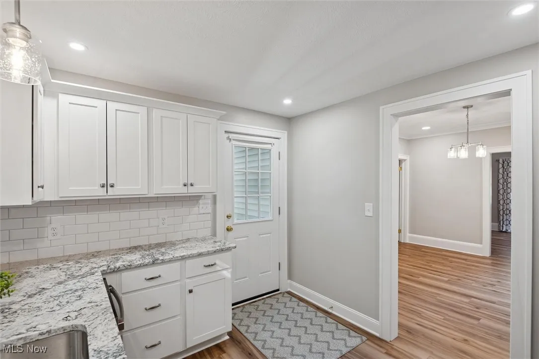 Kitchen featuring hanging light fixtures, white cabinets, light stone counters, dark wood finished floors, and recessed lighting