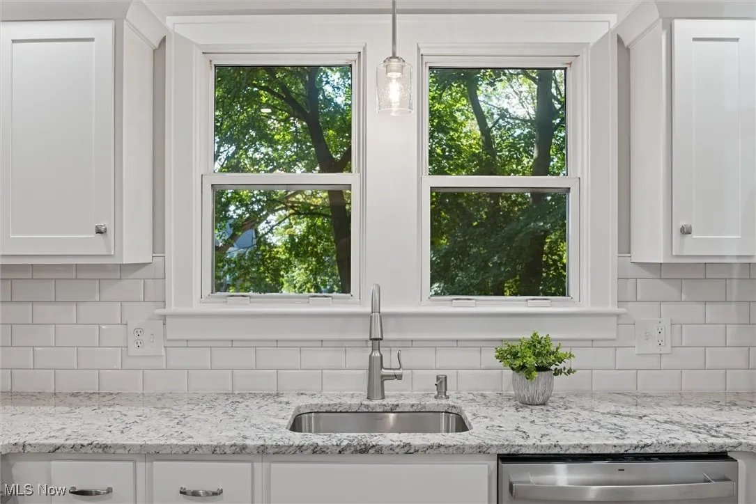 Kitchen with decorative backsplash, light stone countertops, white cabinetry, pendant lighting, and stainless steel dishwasher