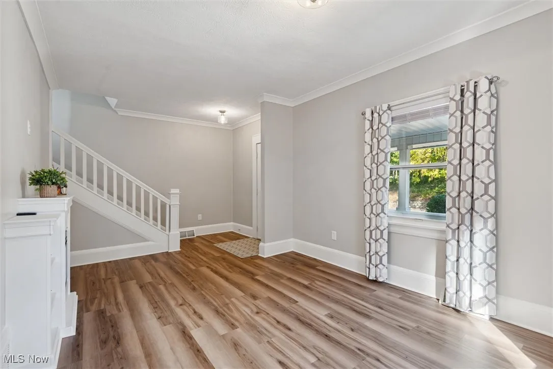Empty room with crown molding, light wood finished floors, and stairway