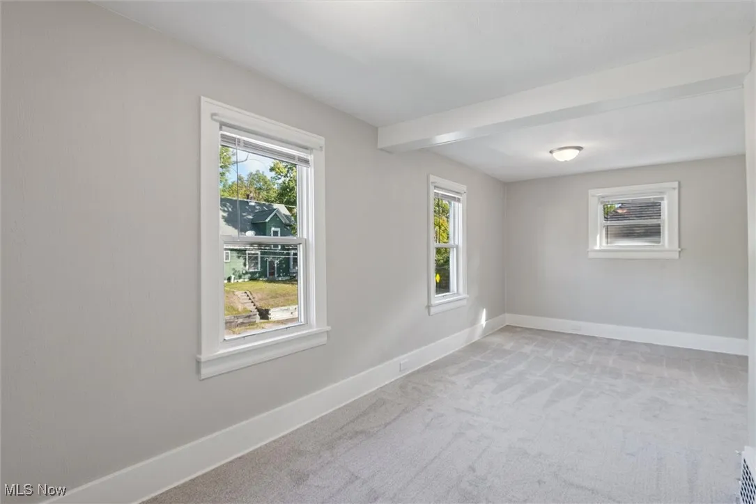 Empty room with light carpet, healthy amount of natural light, and beam ceiling