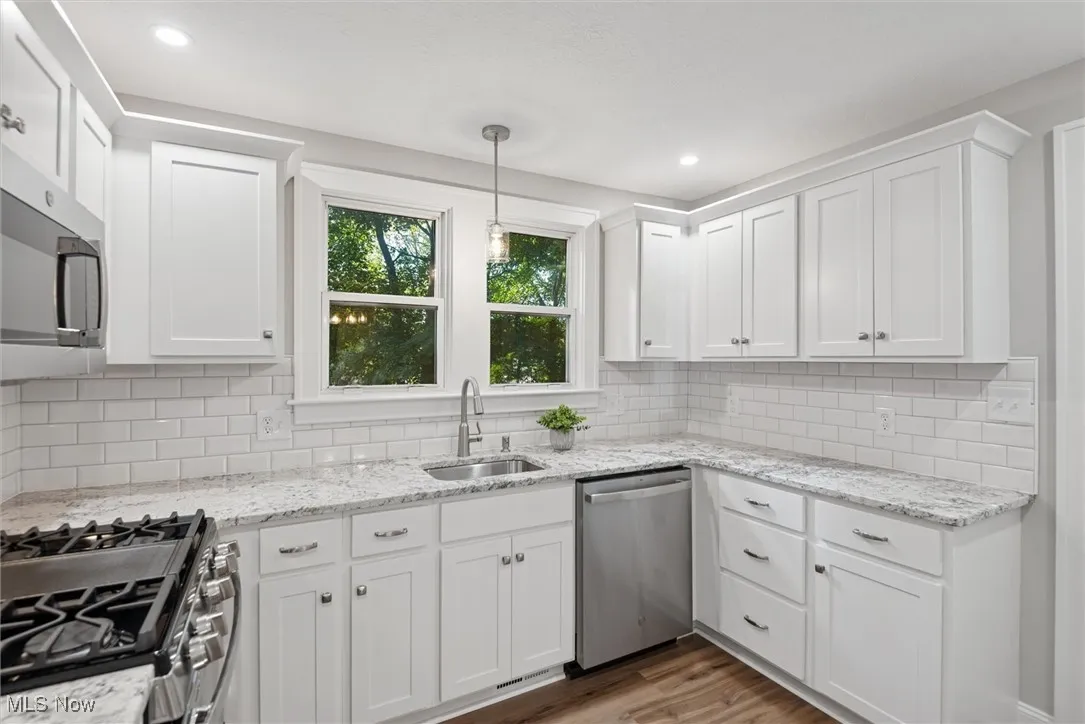 Kitchen featuring hanging light fixtures, appliances with stainless steel finishes, dark wood-type flooring, white cabinets, and light stone counters