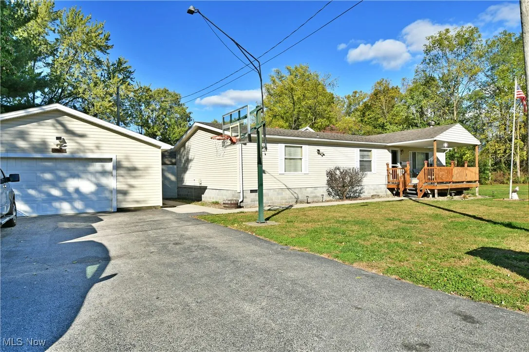 View of property exterior featuring a yard, an outdoor structure, a wooden deck, driveway, and a detached garage