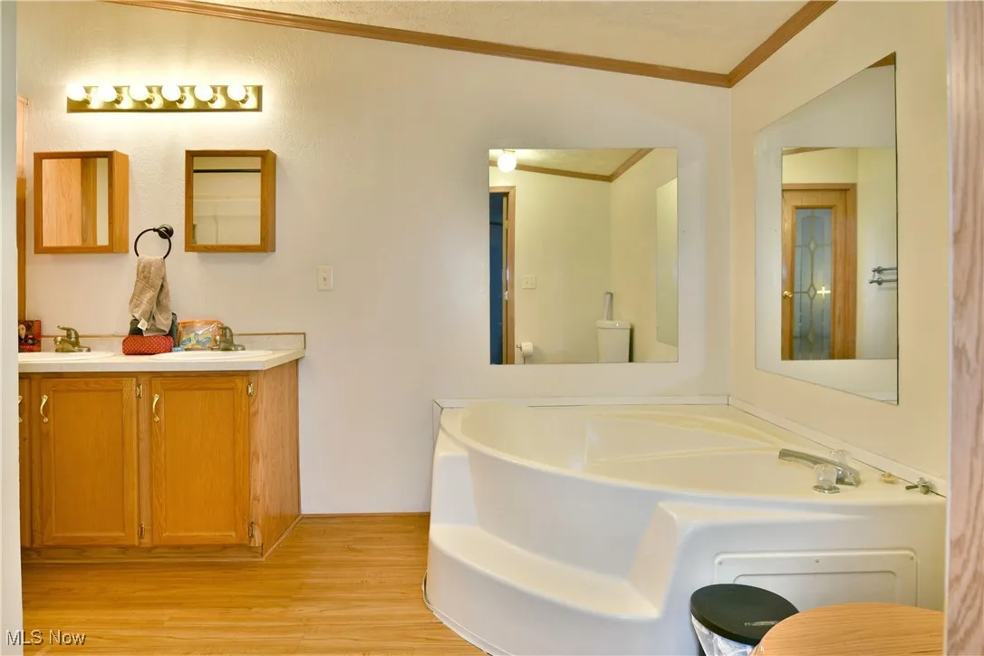 Bathroom featuring a garden tub, light wood finished floors, double vanity, and crown molding