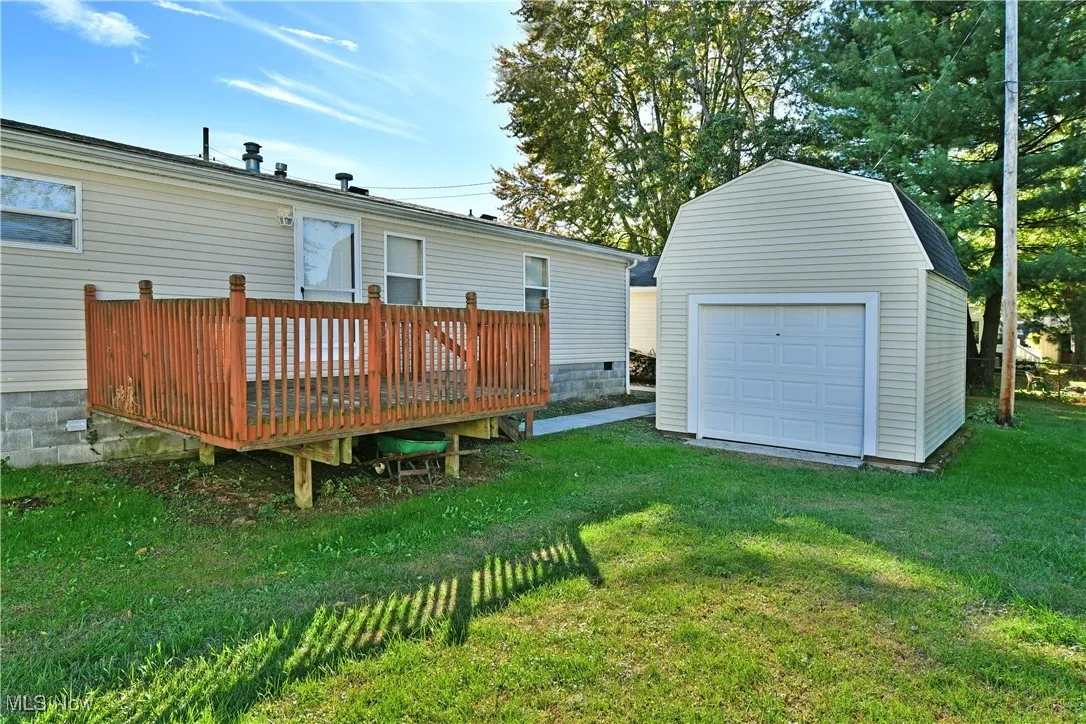 Back of house featuring a yard, a wooden deck, a garage, and an outbuilding