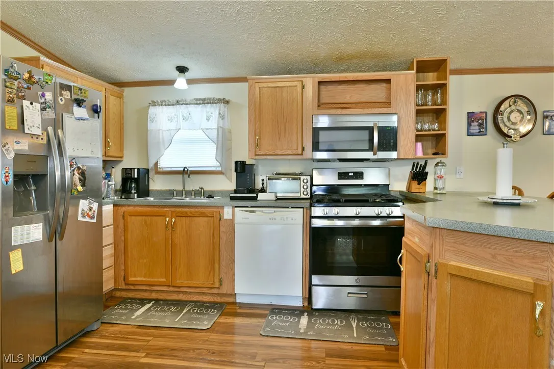 Kitchen with stainless steel appliances, open shelves, a textured ceiling, ornamental molding, and dark wood finished floors